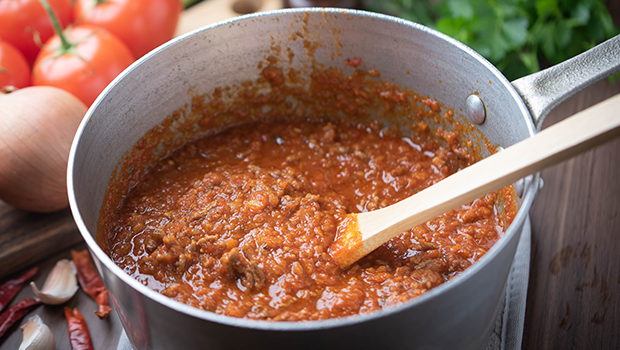 This is an image of a metal pot containing meat sauce with a wooden spoon sticking out.