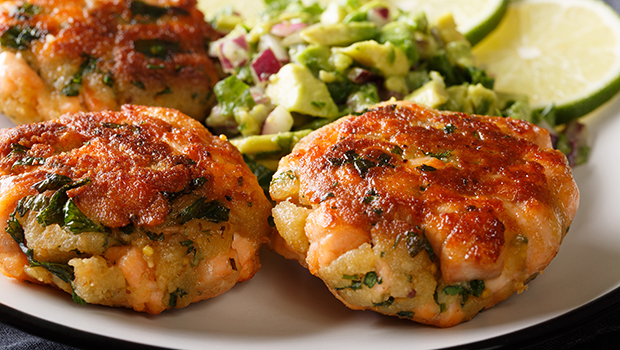 This is a close-up image of cooked salmon cakes with an avocado lime dip and sliced lime.