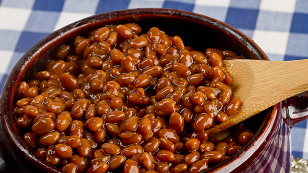 Baked beans in a brown bowl with a wooden spoon sticking out of the bowl