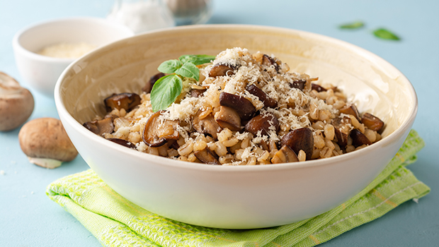 Barley pilaf with cut mushrooms and garnish in a white bowl
