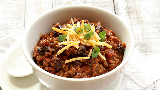 Close-up of beef chili with shredded cheese on top in a white bowl