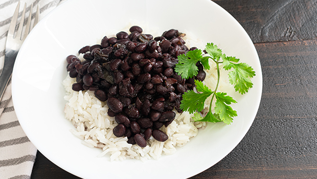 Cooked black beans on white rice with a garnish, all on a white plate