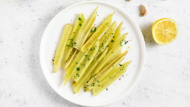 A white plate full of braised celery with garnish