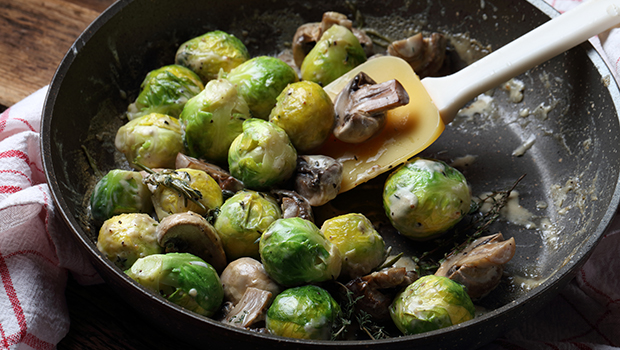 Brussels sprouts and mushrooms in a black skillet with a plastic spatula