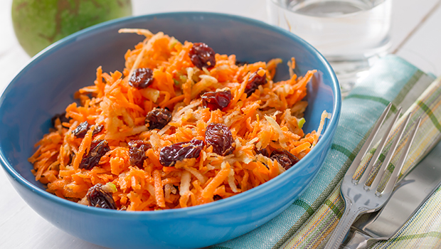 Shredded carrots and raisins in a blue bowl with fork and knife next to it