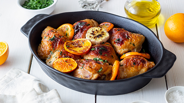 Baked chicken thighs with slices of oranges in a black serving dish