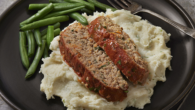 Two slices of meatloaf on mashed potatoes with a side of green beans