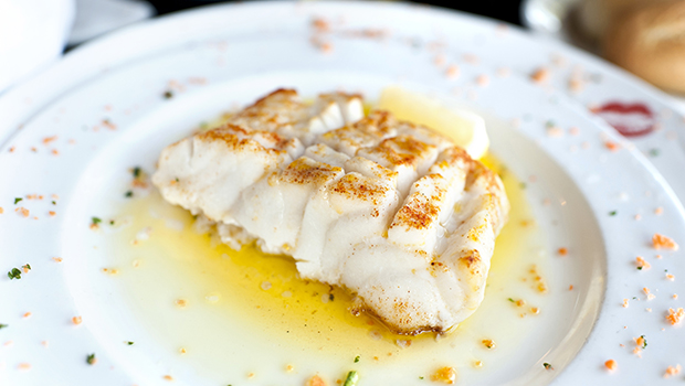 Cooked white fish on a white plate with a lemon wedge