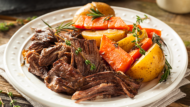 Beef pot roast with carrots and potatoes in a white shallow dish