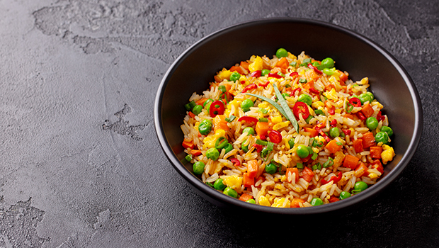 Black bowl containing rice pilaf, corn, peas, carrots, and red pepper