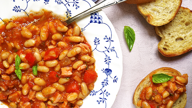 Bowl with white beans and tomato-based sauce with bread crackers next to it
