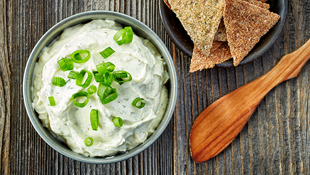 Small steel bowl containing a white dip with chives on top and whole grain tortilla chips on the side