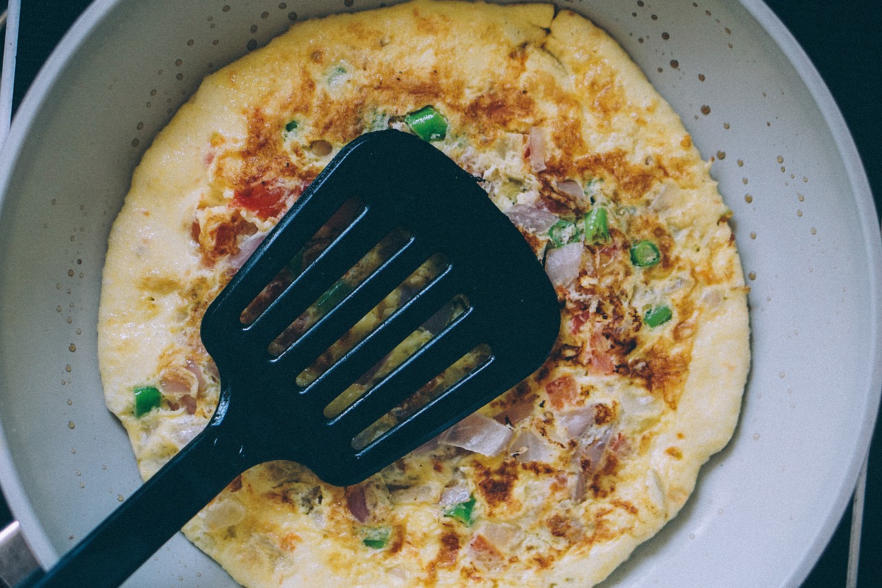 Omelet in a pan with a black spatula pressing down on the omelet