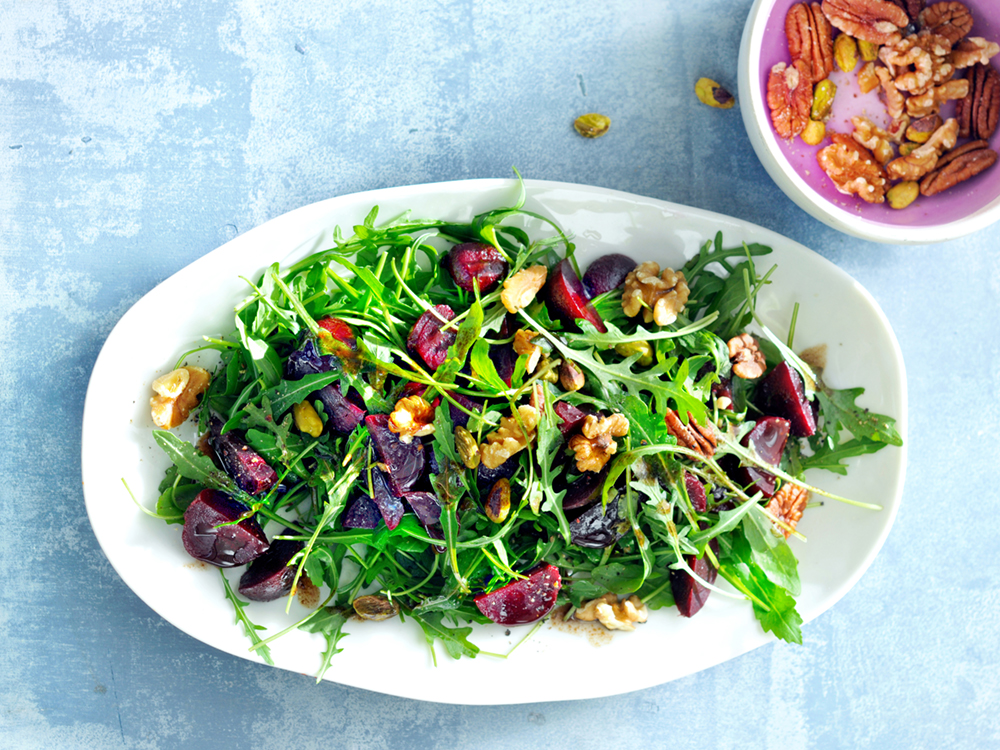 Arugula, beets, walnuts, pecans, and balsamic dressing in a shallow white bowl