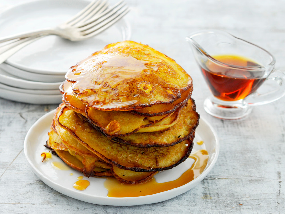Stack of eight pancakes with syrup on top and in a pourer on the side