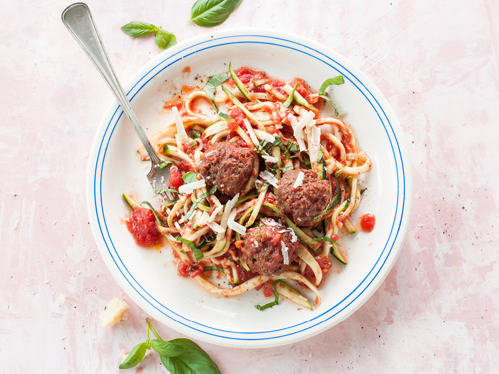 Top-down view of zucchini noodles and three meatballs in a tomato-based sauce
