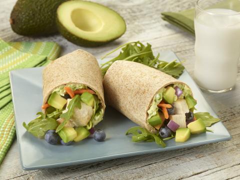 Rolled wheat tortilla containing avocado, chicken, blueberries, carrots, and arugula on a square blue plate