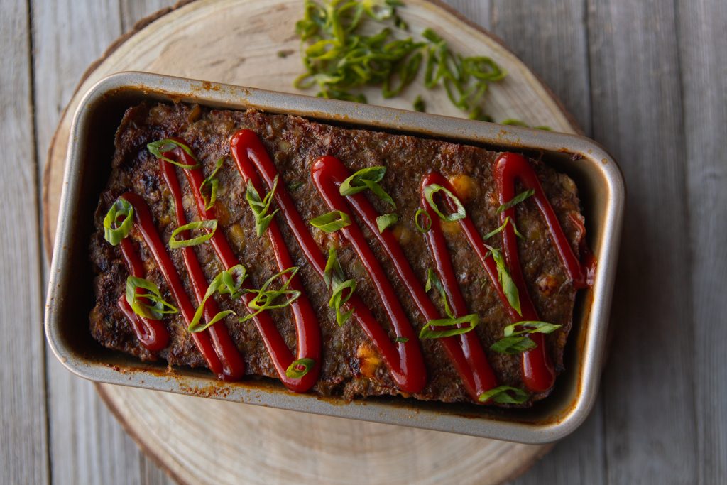 Top-down view of meatloaf in a baking dish with a ketchup drizzle and garnish