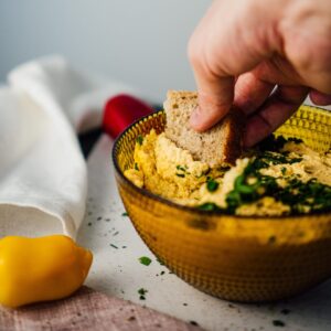 person dipping a piece of bread into a bowl of hummus
